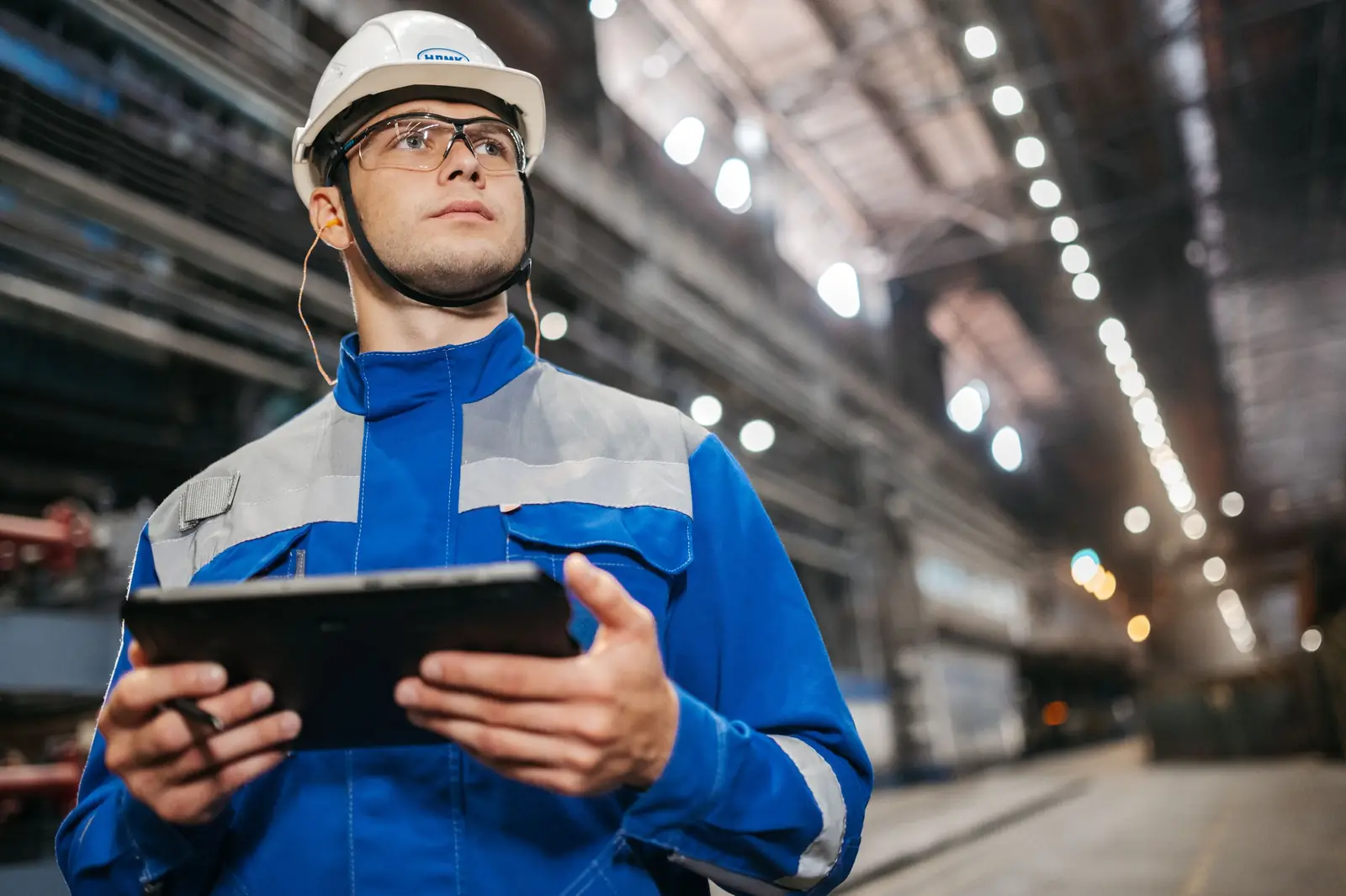 Ingenieur mit Schutzhelm und Schutzbrille hält ein Tablet in einer Werkshalle